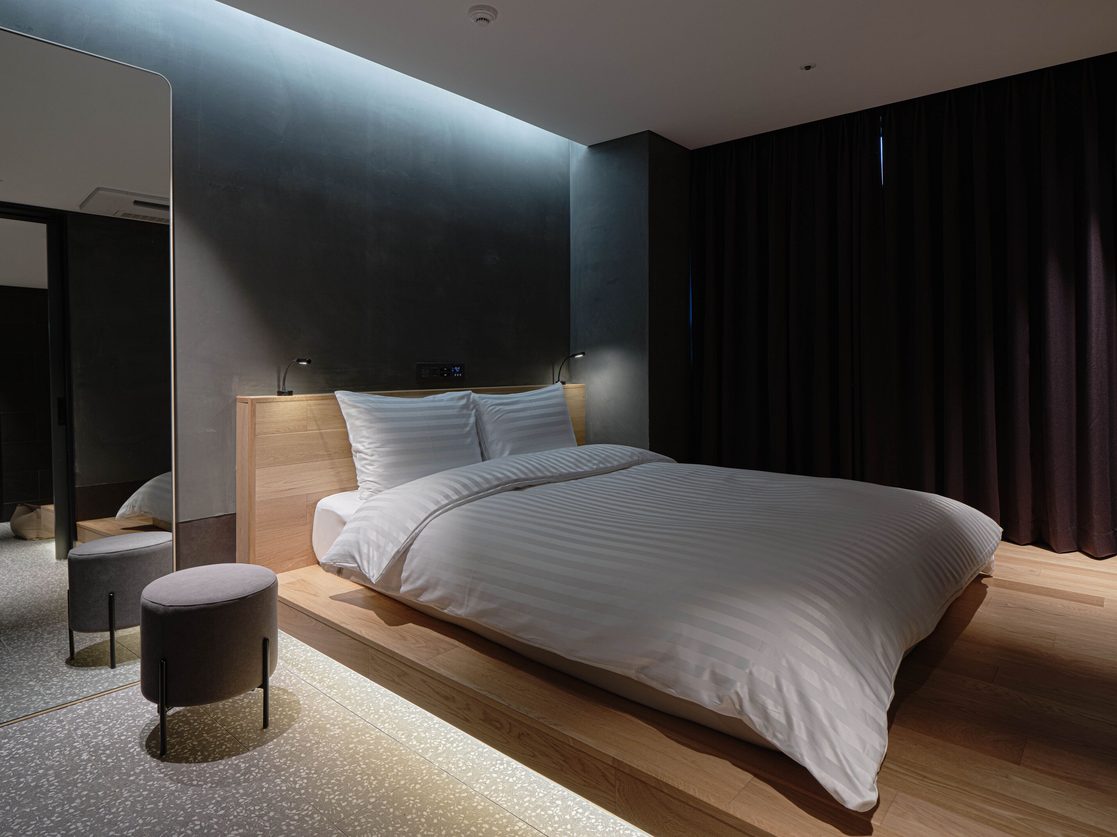 Un dormitorio moderno con una cama grande, una mesita de noche, un espejo y una cortina oscura.