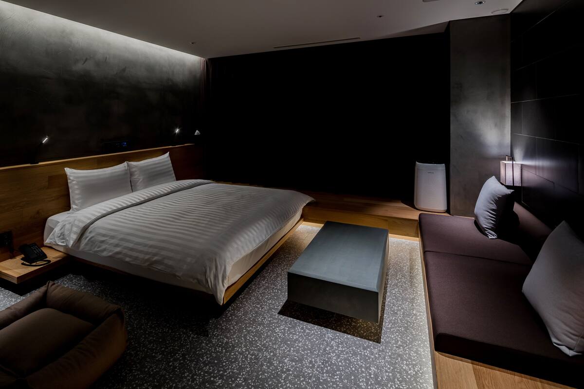 A modern hotel room with a large bed, a sofa, a small table, and a bedside lamp.
