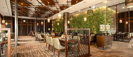 A modern restaurant with wooden ceiling panels, hanging pendant lights, and a green wall with plants.