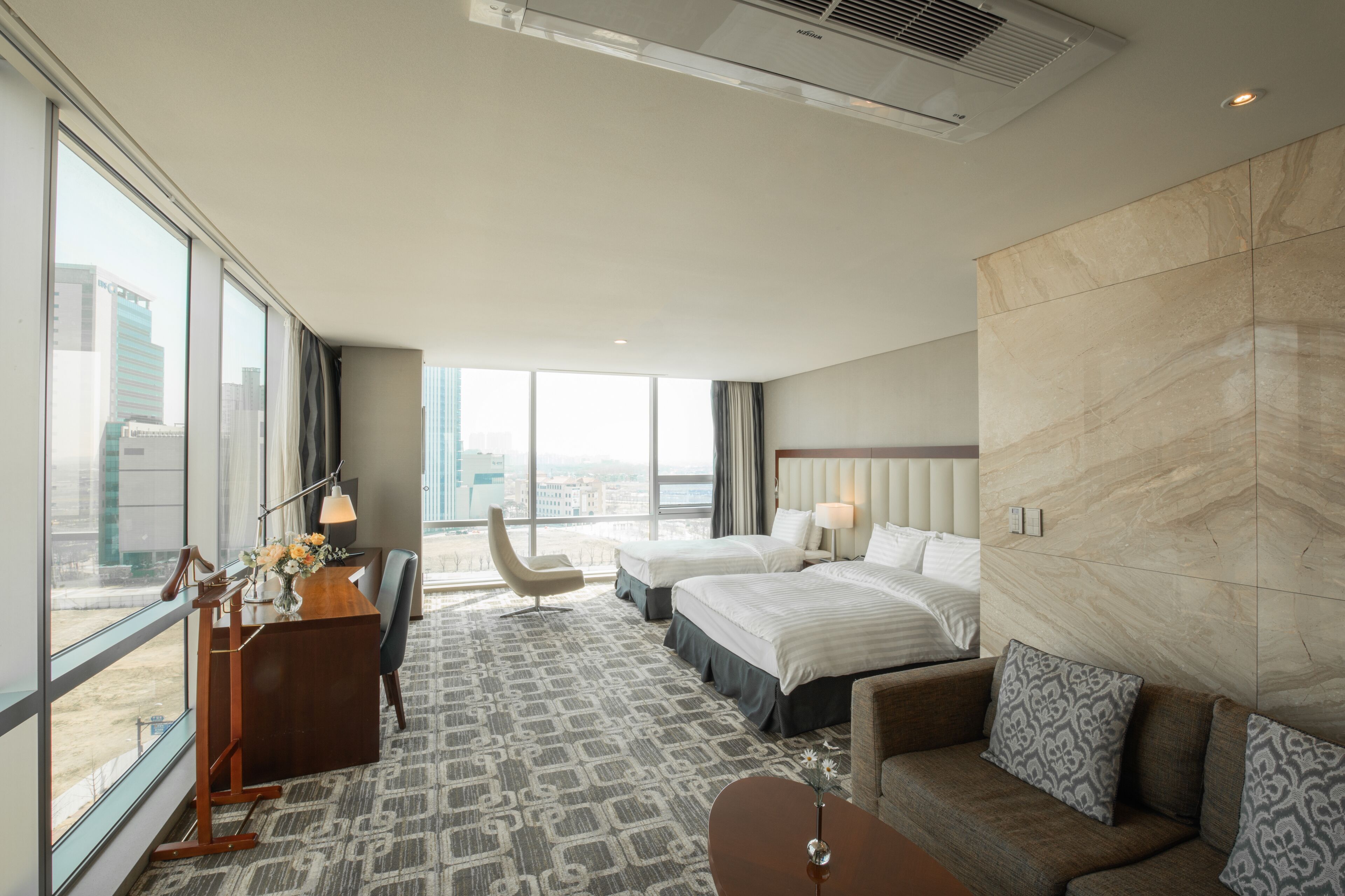 Une chambre d’hôtel dotée d’une grande fenêtre, d’un bureau avec une lampe, d’un lit, d’un canapé et offrant une vue sur la ville.