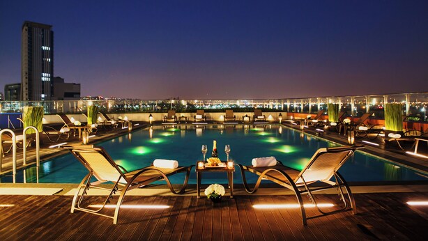 A rooftop pool with lounge chairs and a table set for two, overlooking a cityscape at dusk. - Sono Calm Goyang (Goyang)