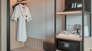 A compact hotel room with a built-in seating area, a minibar, and a robe hanging on the wall.