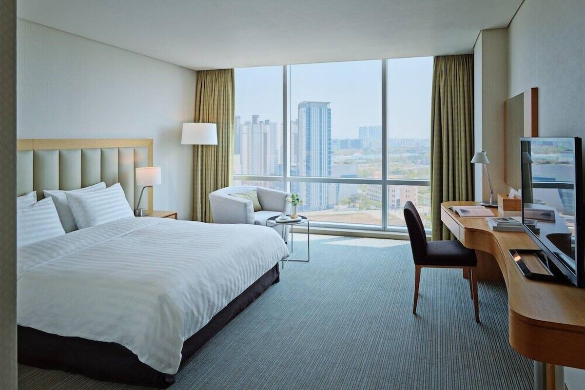 A hotel room with a large bed, a desk with a computer, a chair, and a view of the cityscape.