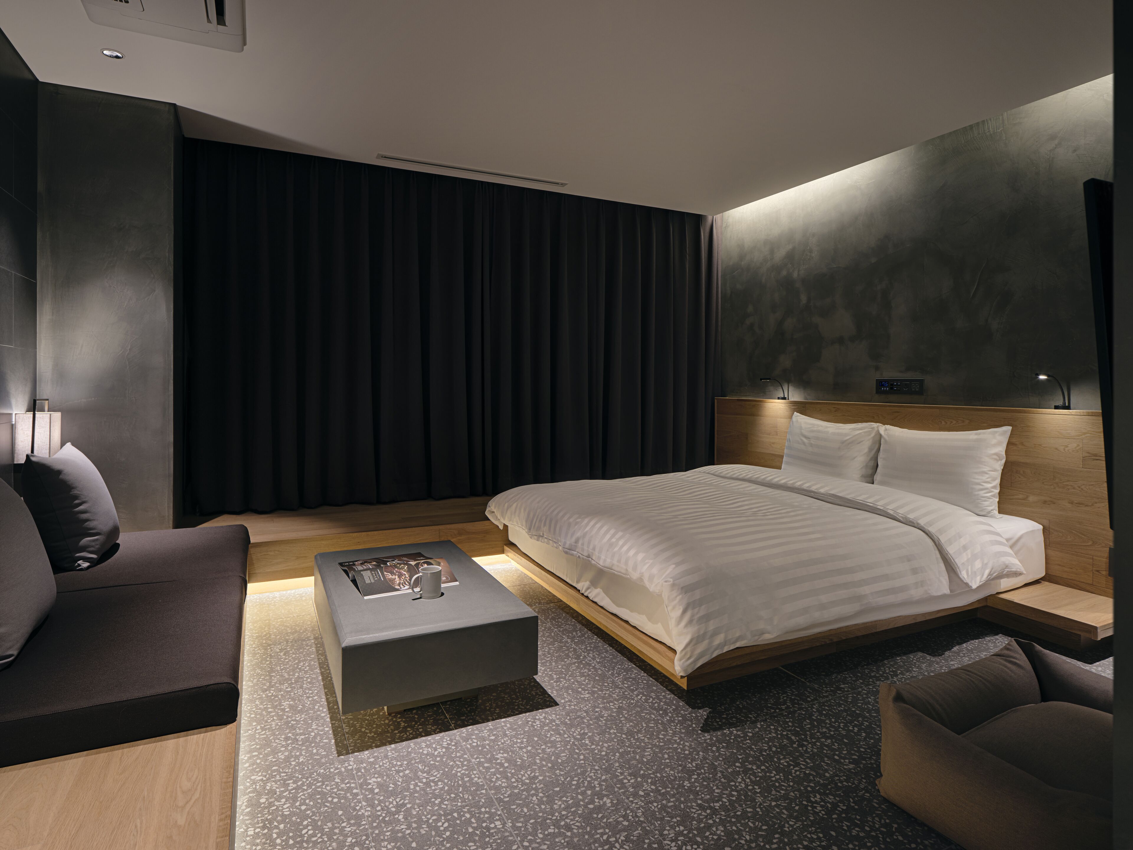 Una habitación de hotel moderna con una cama grande, un sofá, una mesa de centro y un televisor montado en la pared.