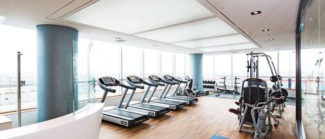 Un gimnasio moderno con cintas de correr, máquinas de ejercicio y una colchoneta azul.