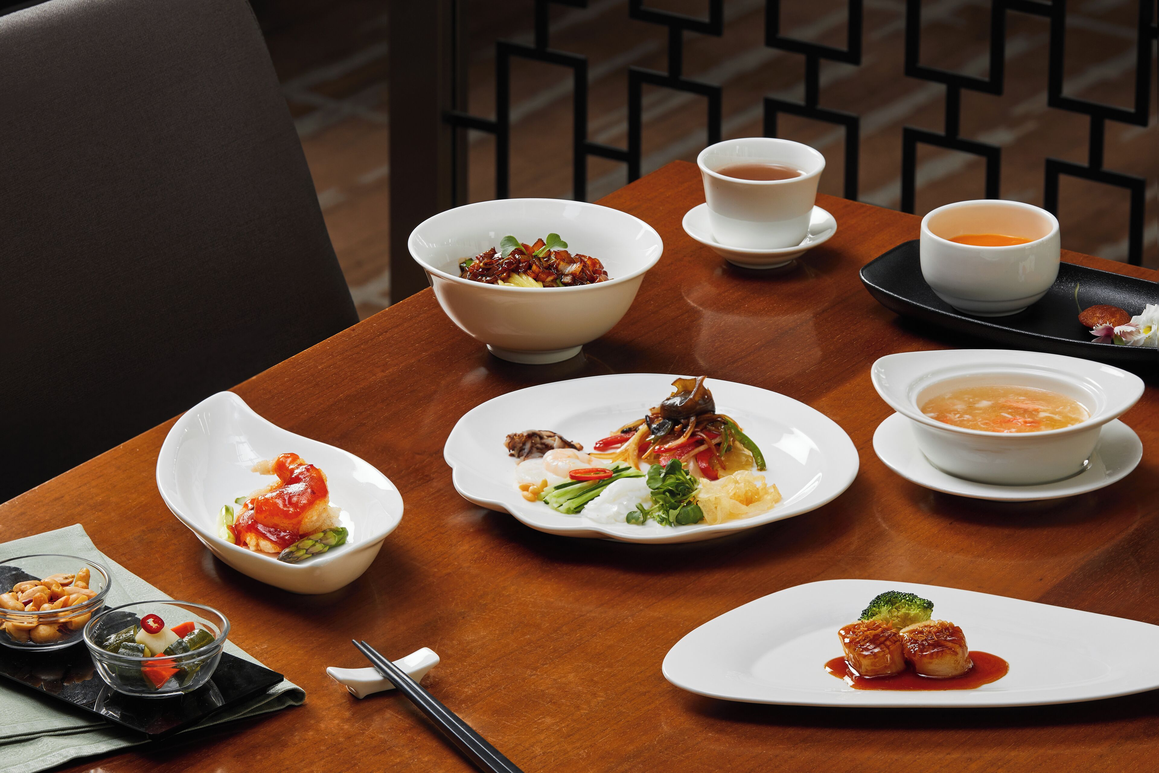 A dining table with various dishes, including a bowl of soup, a plate with vegetables, and a plate with meat.