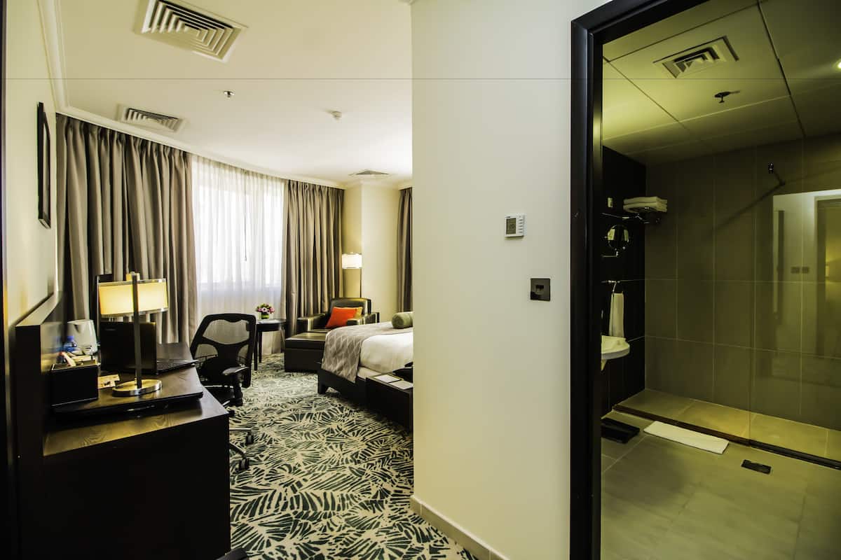 A hotel room with a bed, desk, chair, and a shower area.