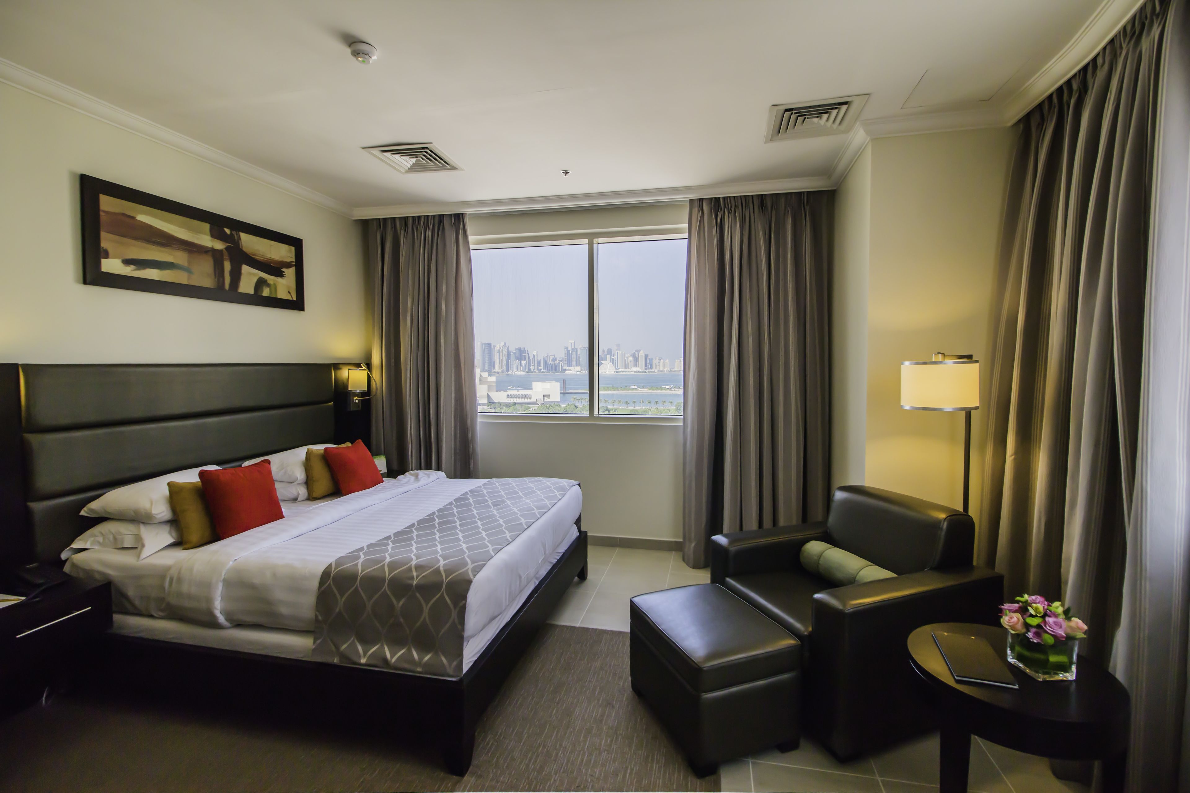 A hotel room with a large bed, a sofa, a small table, and a view of the city skyline.