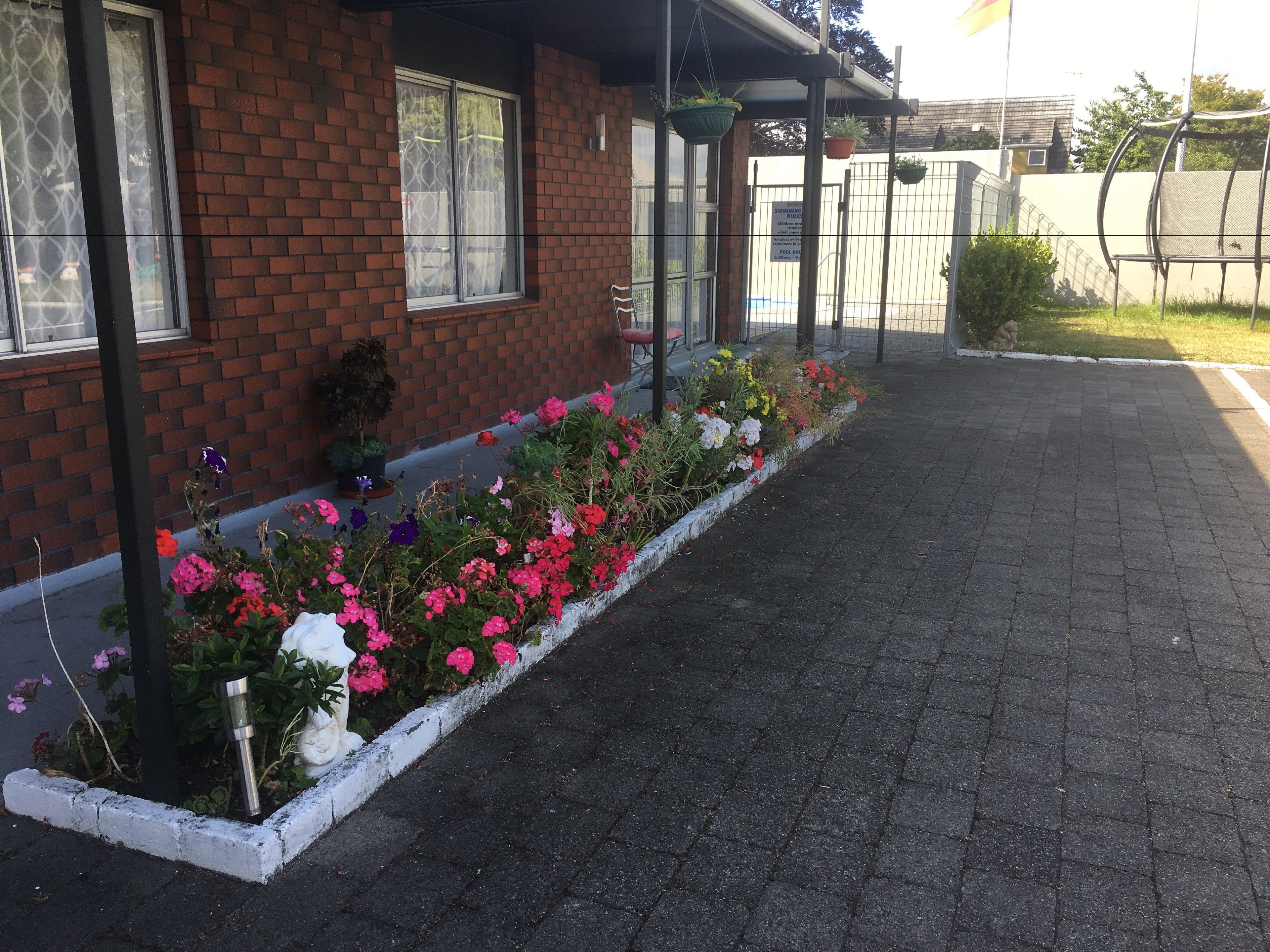 Edificio de ladrillo con un camino empedrado y una jardinera con flores rosadas y blancas.