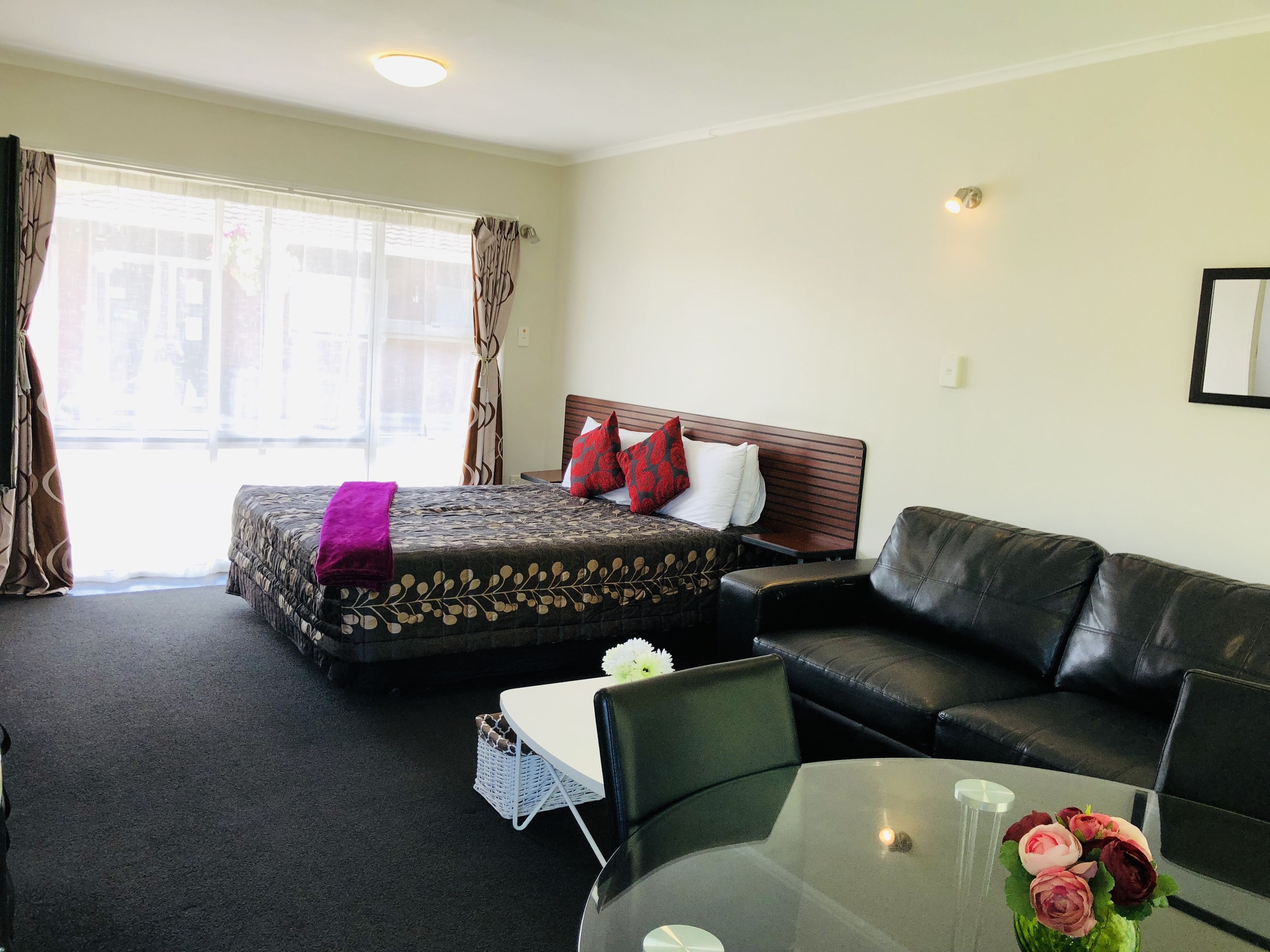 A hotel room with a bed, a sofa, a glass table, and a view of the street.