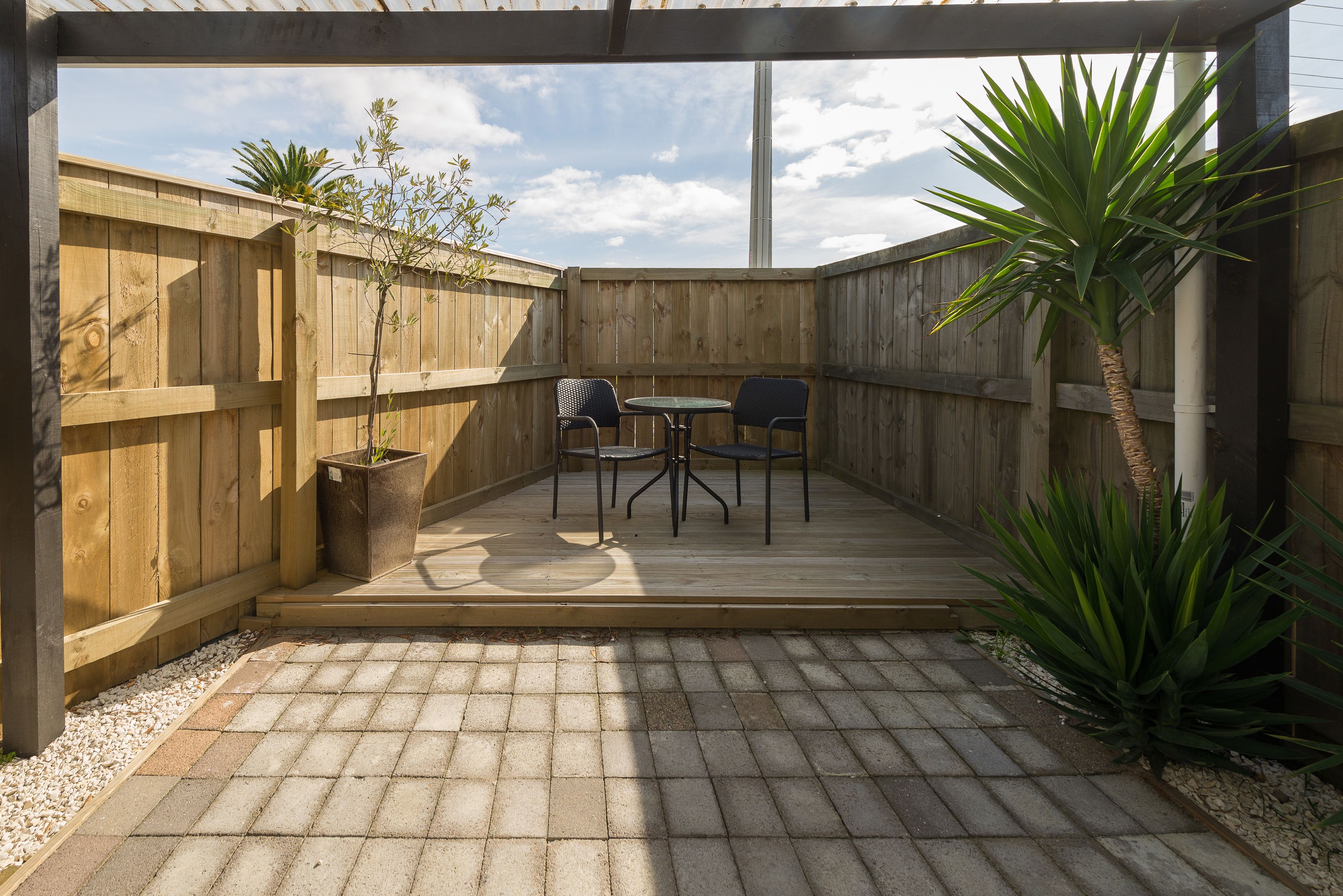 Una terraza de madera con una mesa y sillas, rodeada por un cerco de madera, y con una planta en maceta.