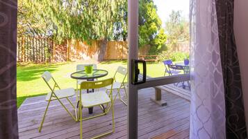An outdoor patio with a round table and chairs, a wooden deck, and a view of a backyard with a wooden fence and trees.