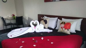 A hotel room with a bed, a red throw blanket, and a heart-shaped towel arrangement. - Red Rock Thermal Motel (Rotorua)