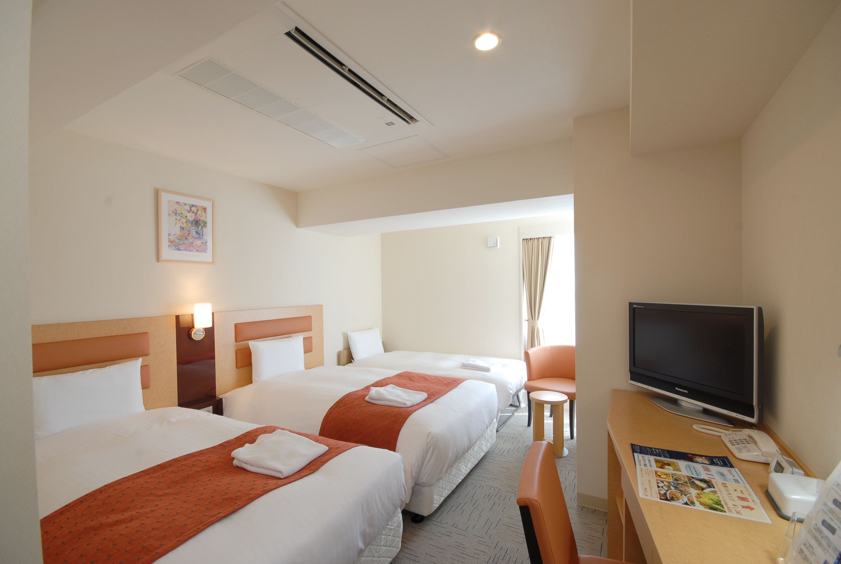 A hotel room with two beds, a desk with a TV, and a small table.