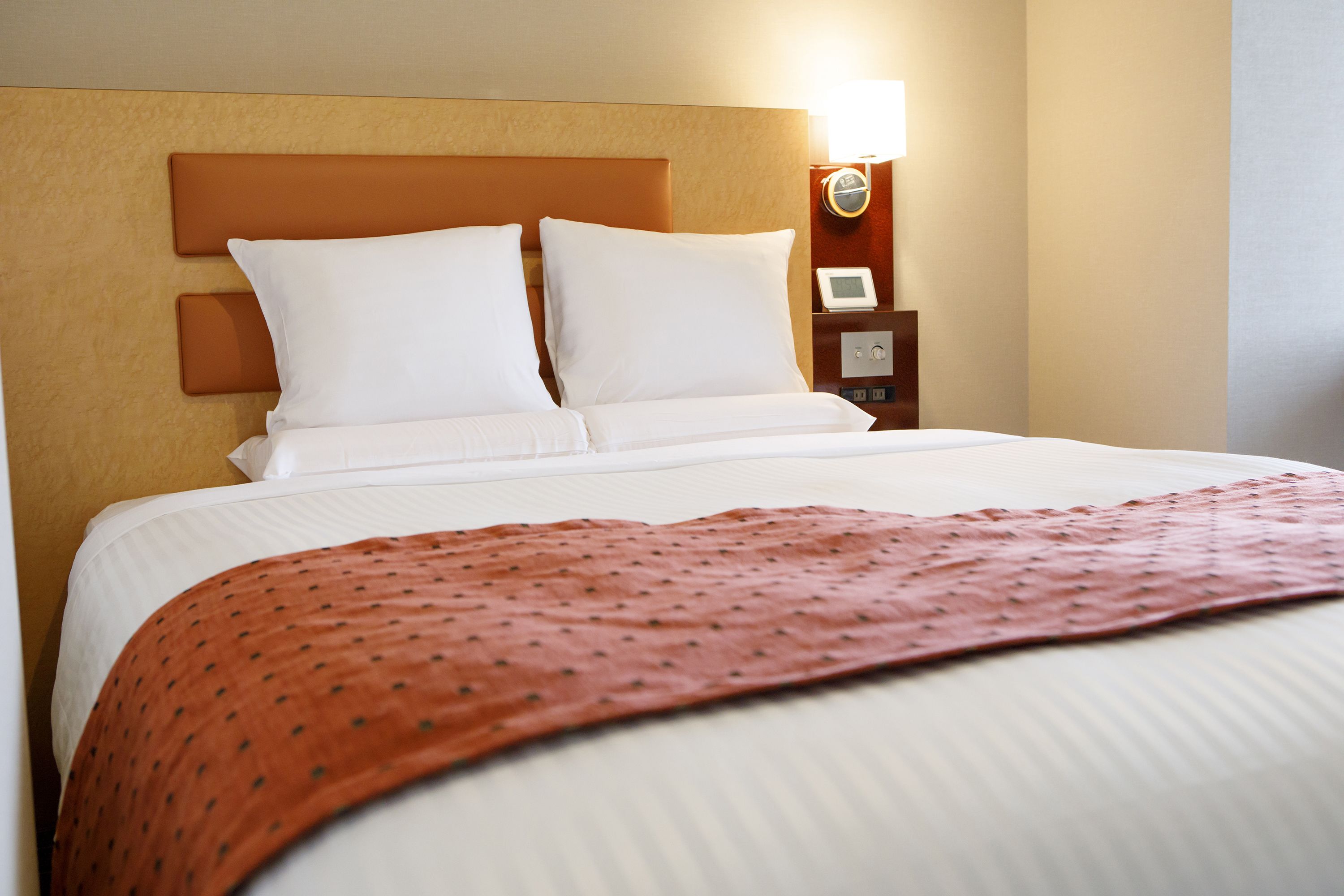 A neatly made bed with white linens and a brown patterned throw blanket.