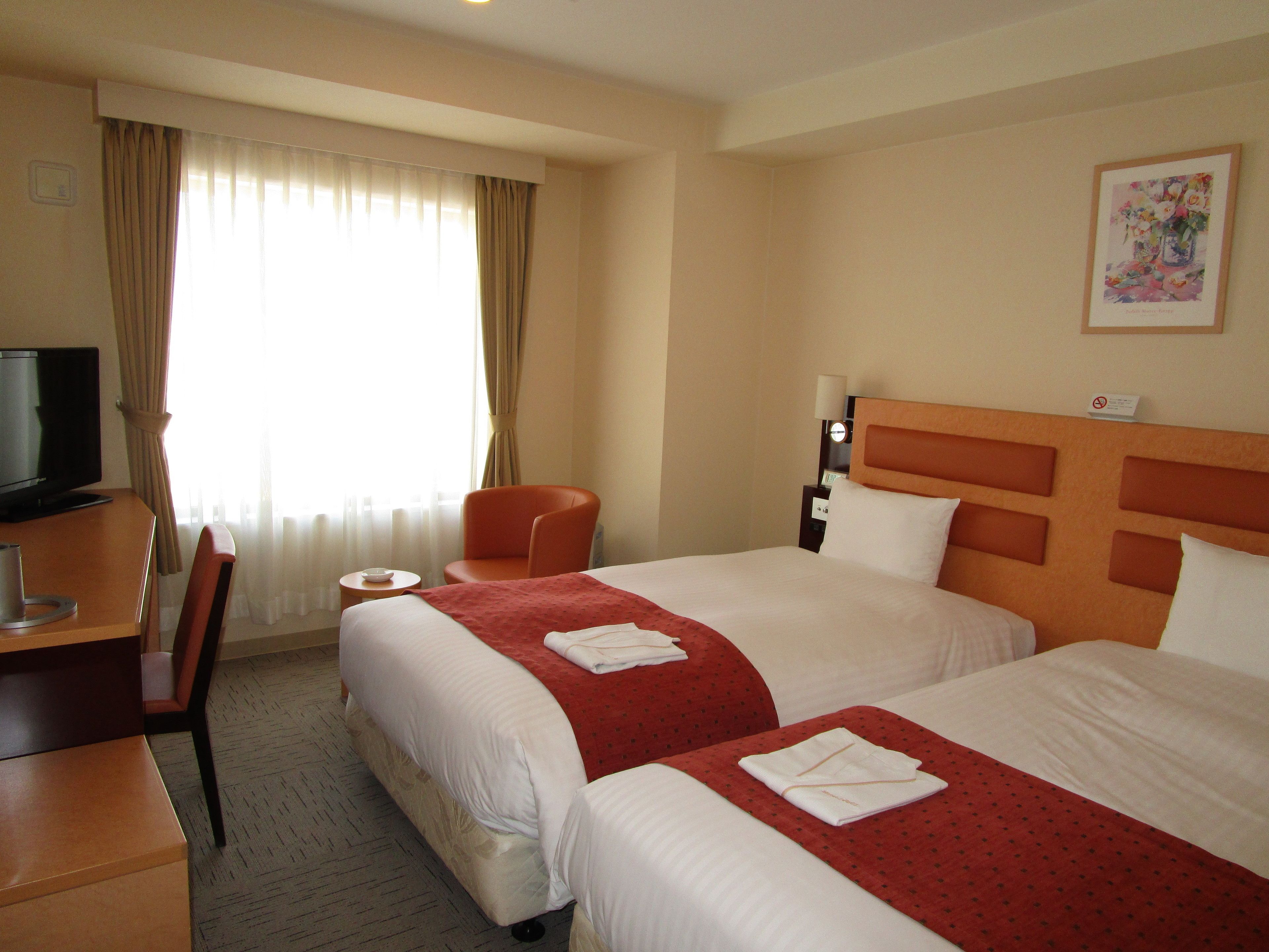 A hotel room with two beds, a desk with a TV, a chair, and a window with curtains.