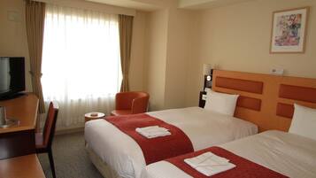 A hotel room with two beds, a desk with a TV, a chair, and a window with curtains.