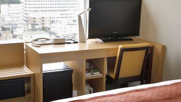 A hotel room with a wooden desk, a computer, a telephone, and a bed with a red blanket.