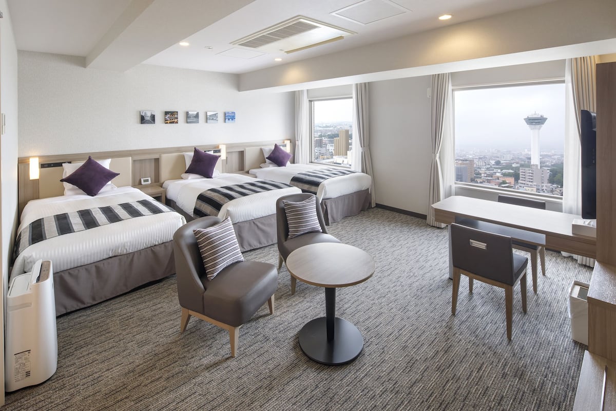 Habitación de hotel con tres camas, una mesa redonda y vista a la ciudad.