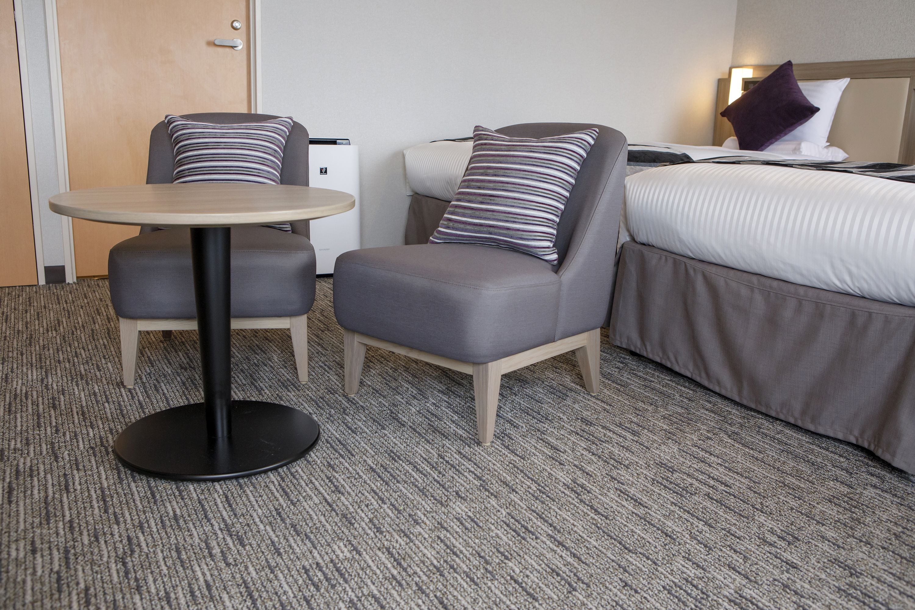 A hotel room with a bed, two armchairs, a small round table, and a bedside table.