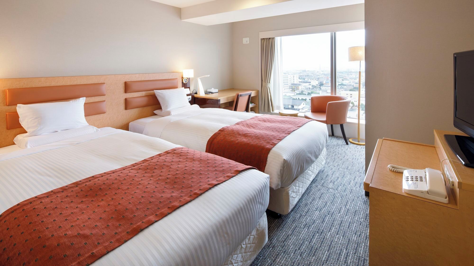 Ett hotellrum med två sängar, ett skrivbord, en stol, en tv och en telefon.