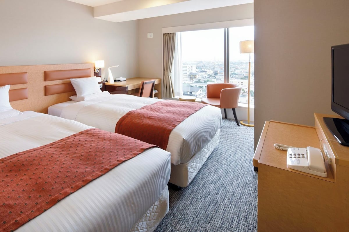 Una habitación de hotel con dos camas, un escritorio, una silla, un televisor y un teléfono.