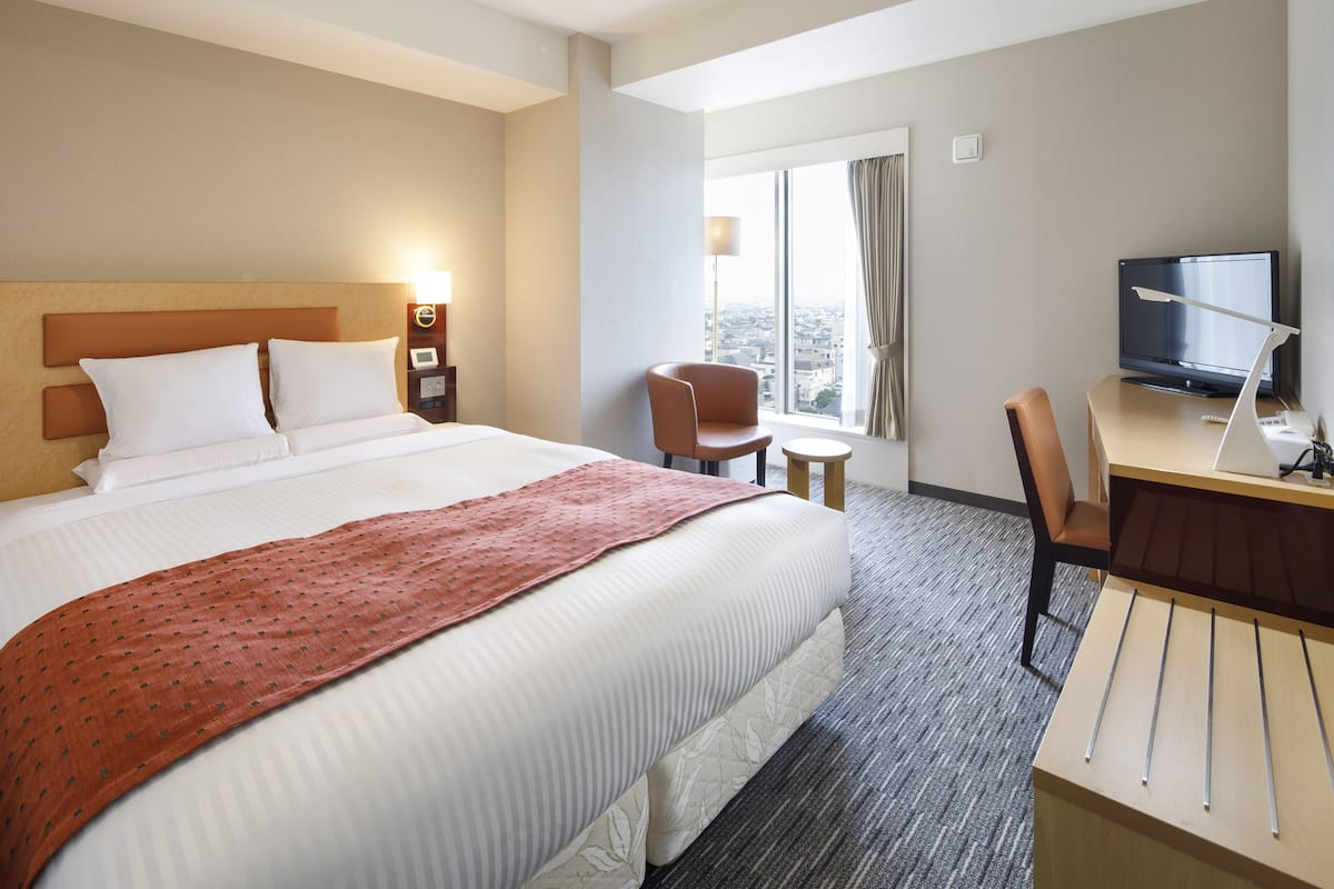 Habitación de hotel con una cama grande, un escritorio con computadora, una silla y un televisor.