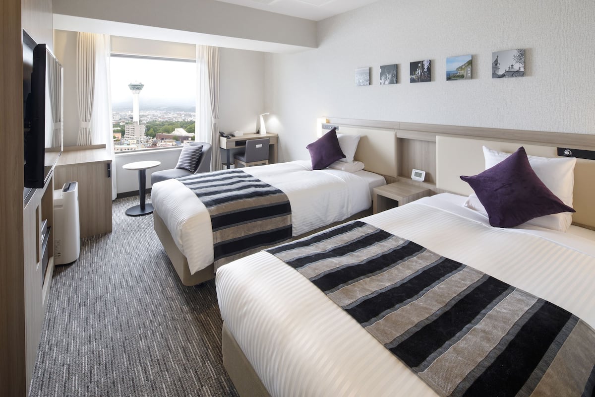 Habitación de hotel con dos camas, un escritorio, una televisión y vistas a una torre.