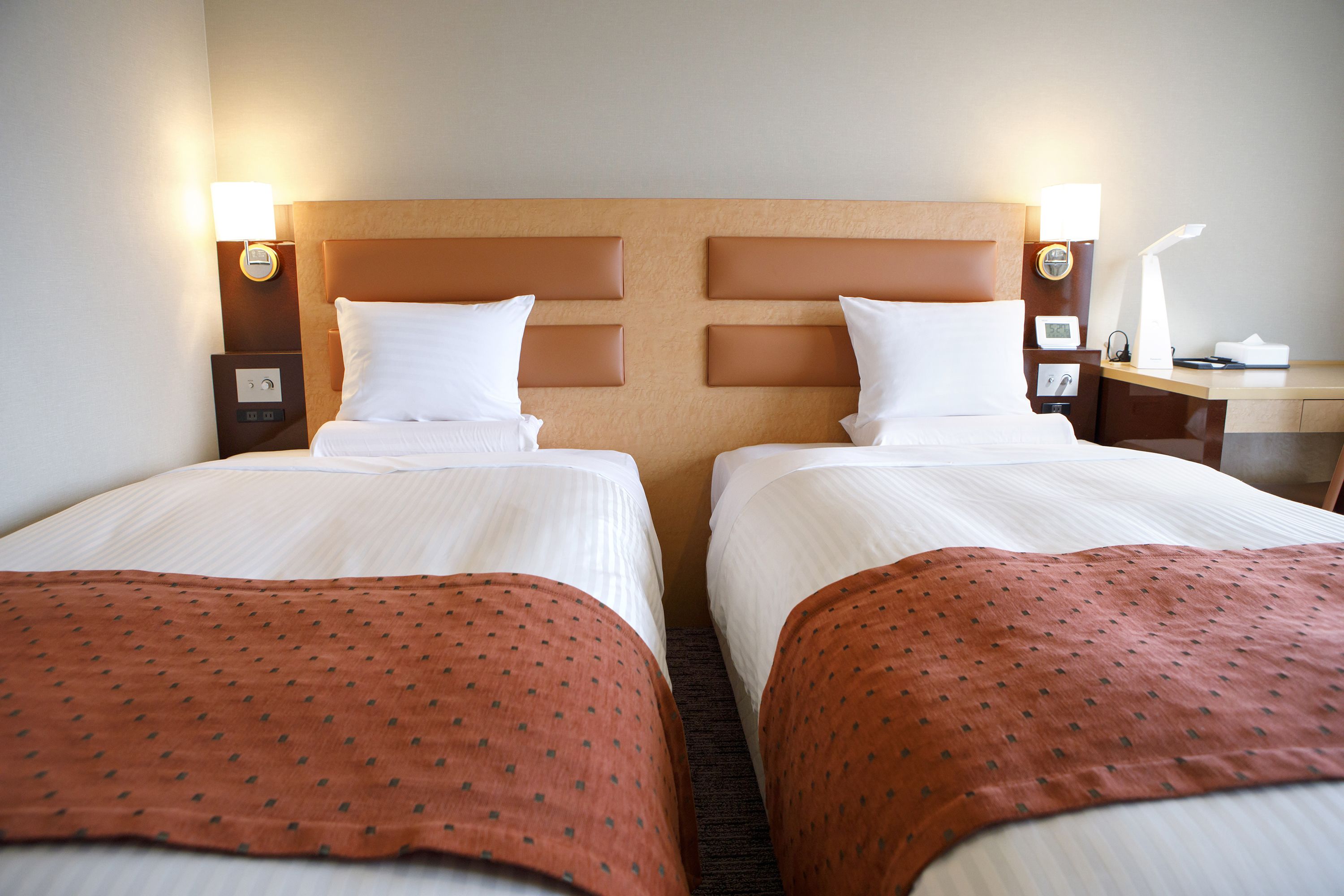 A hotel room with two beds, each with a headboard, a nightstand, a lamp, and a clock.