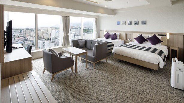 Ein modernes Hotelzimmer mit einem großen Bett, einer Couch, einem Schreibtisch und Blick auf die Stadt.
