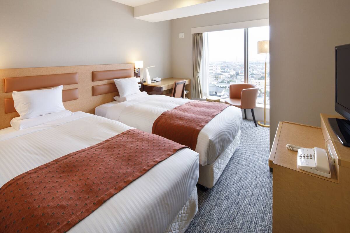Una habitación de hotel con dos camas, un escritorio, una silla, un televisor y un teléfono.
