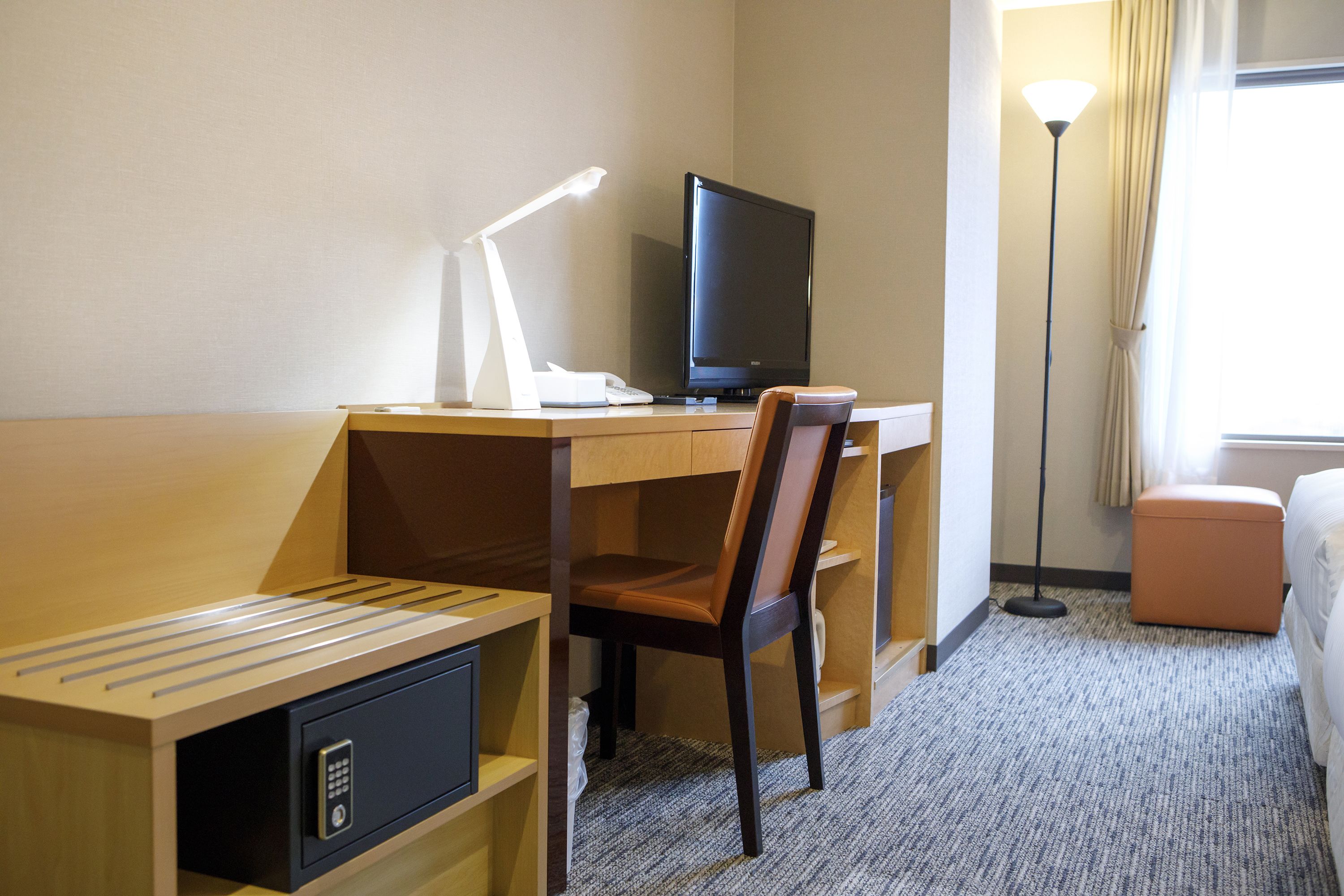 A hotel room with a desk, chair, television, lamp, and a bed.