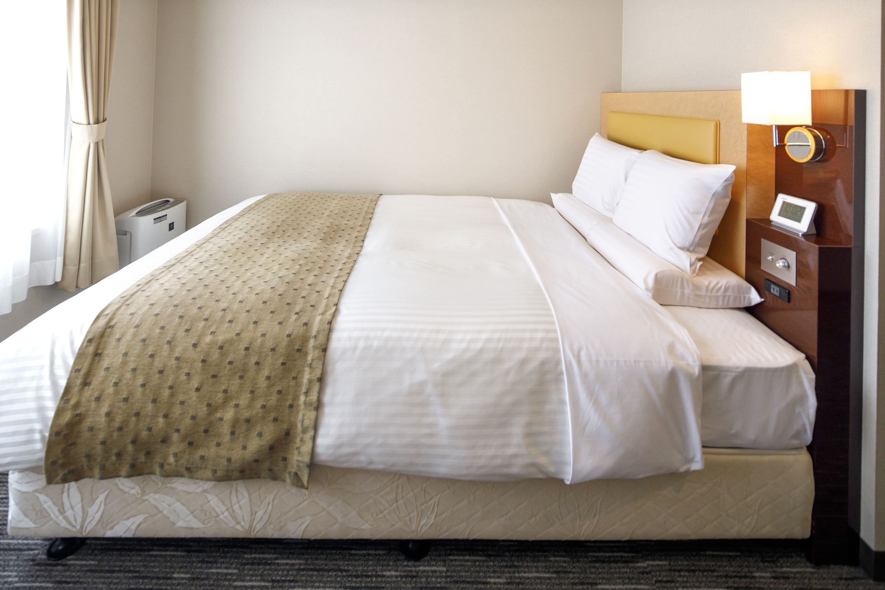 A hotel room with a bed, a nightstand, a lamp, and a thermostat.