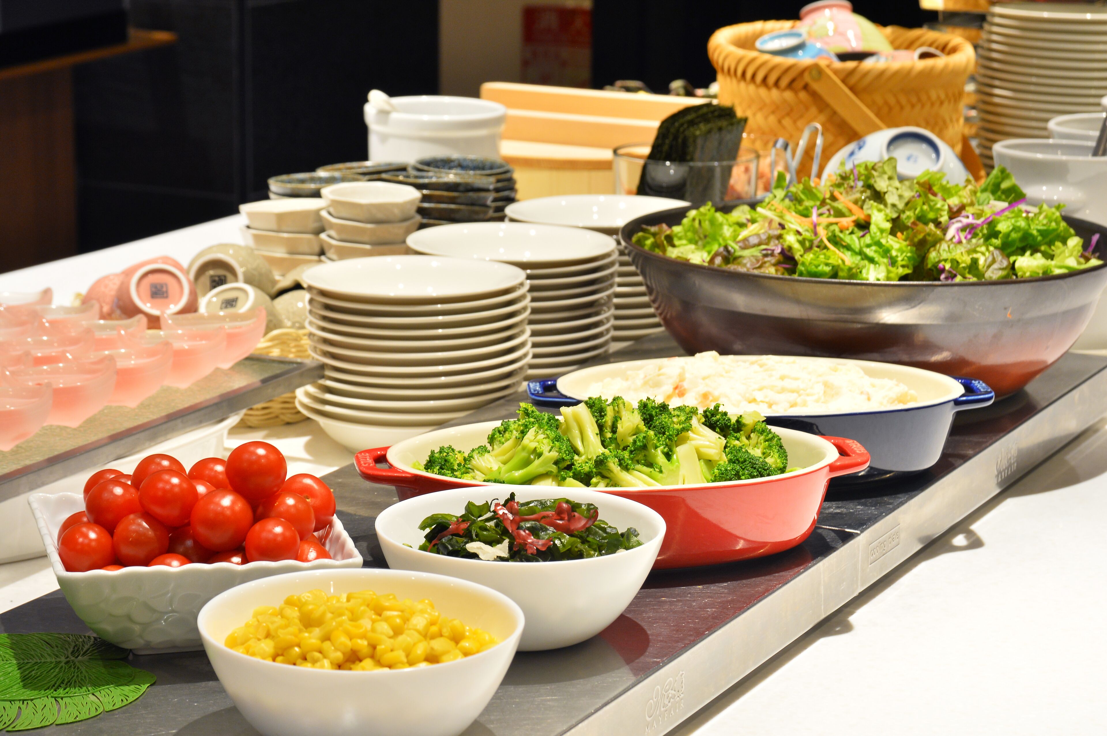 A buffet table with various dishes including salads, broccoli, and corn.