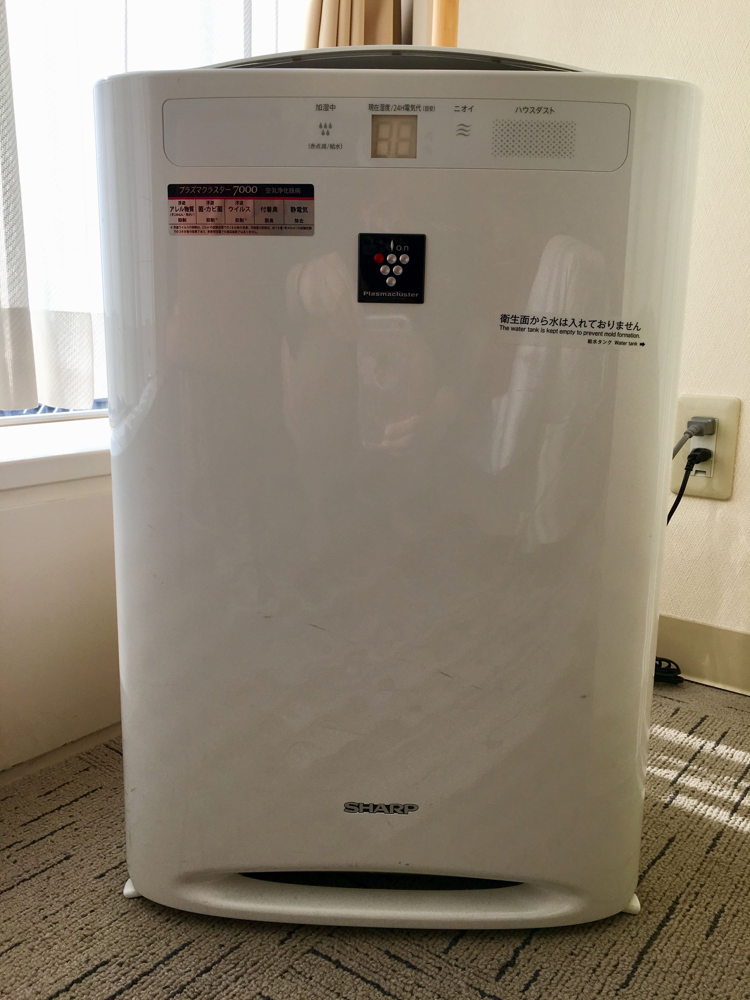 A white air conditioning unit with a digital display, a control panel, and a label indicating it is a Sharp brand.