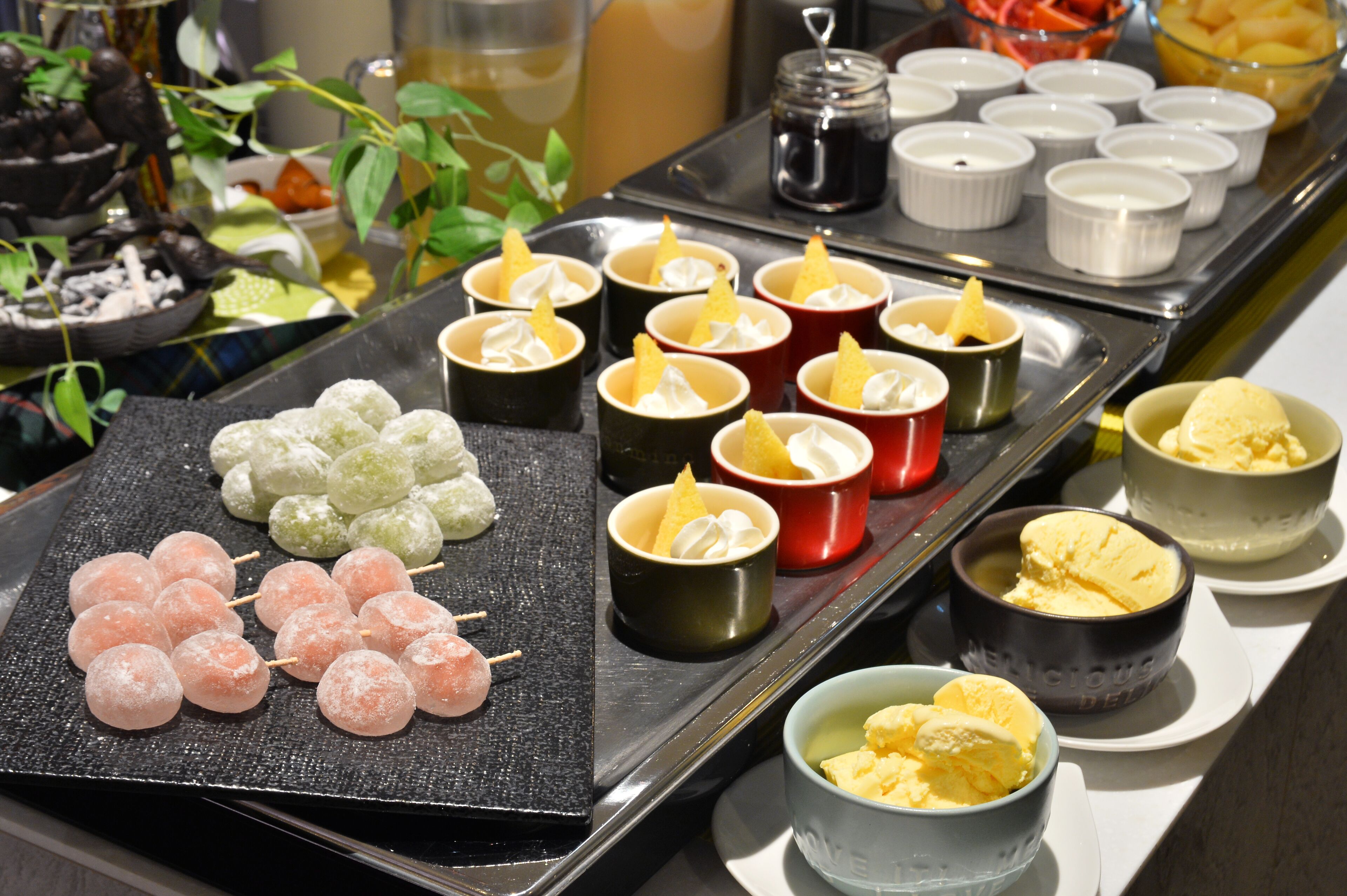 Een buffet met diverse gerechten, waaronder spiesjes, kleine kopjes dessert en kommen met ijs.