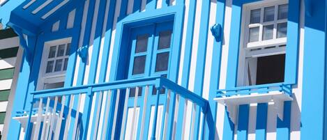 A building with a blue and white striped facade, a balcony with a railing, and multiple windows.