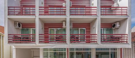 Un edificio de varios pisos con balcones, unidades de aire acondicionado y un cielo despejado.