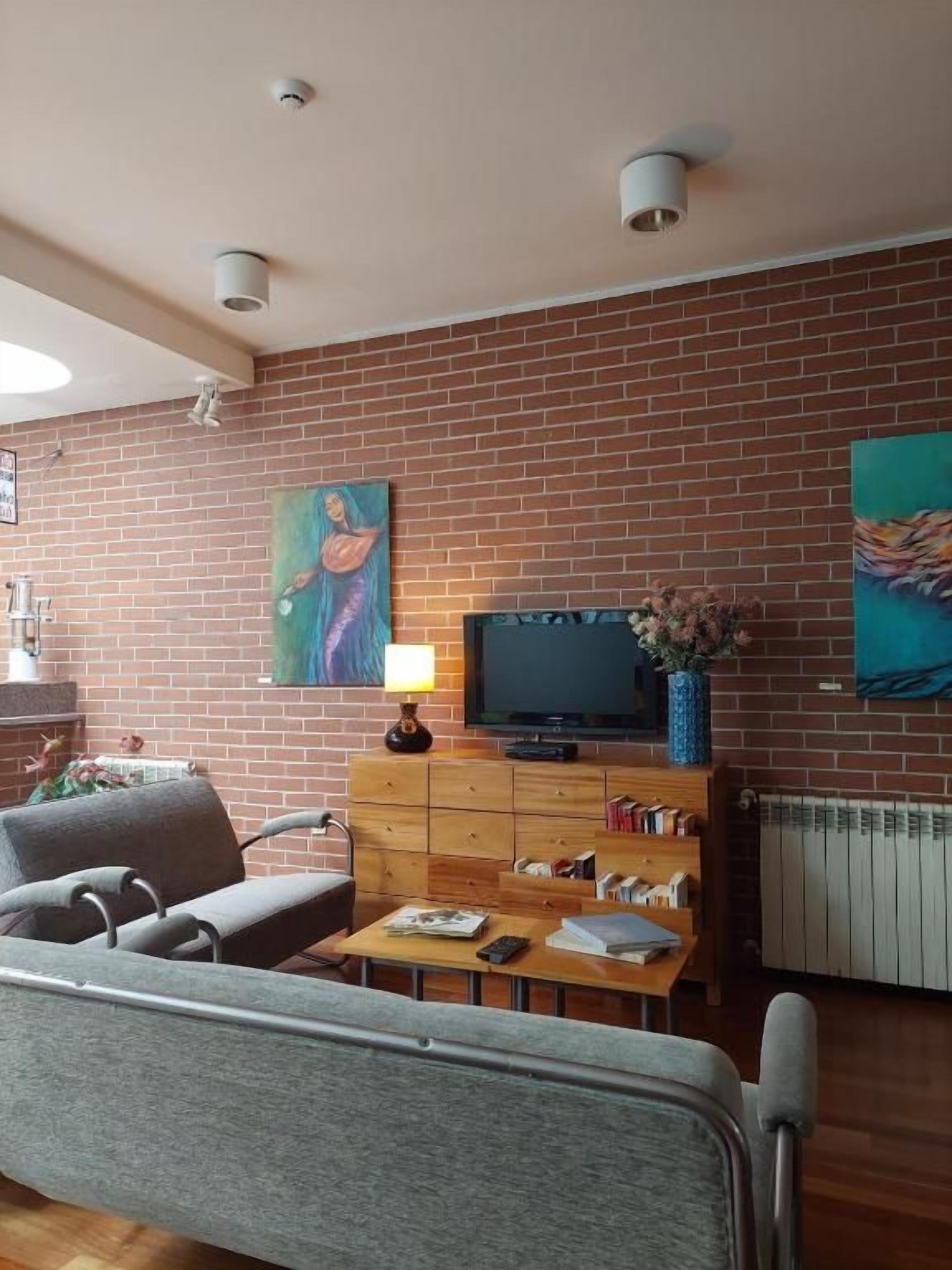 Una sala de estar con pared de ladrillo, televisor, mueble de madera y sofá.