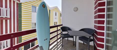 A balcony with a surfboard, two chairs, and a table.