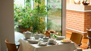 A table set for breakfast with tea and pastries, a brick wall, and a view of greenery. - Costa Nova Hotel (Ilhavo)