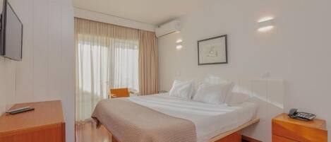 A hotel room with a bed, bedside tables, a television, and a window with curtains.