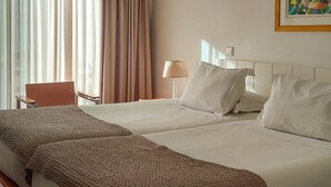 A hotel room with a large bed, a bedside table, a lamp, an air conditioning unit, and a window with curtains. - Costa Nova Hotel (Ilhavo)