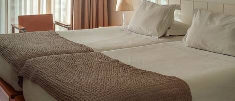 A hotel room with a large bed, a bedside table, a lamp, an air conditioning unit, and a window with curtains.
