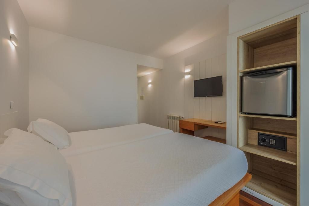 Een hotelkamer met een bed, een bureau, een aan de muur bevestigde televisie en een inbouwkoelkast.