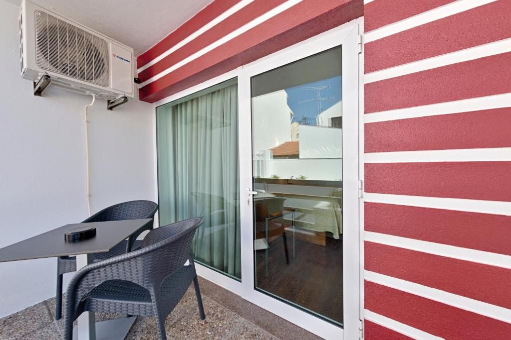 A balcony with a table and chairs, a sliding glass door, and an air conditioning unit.