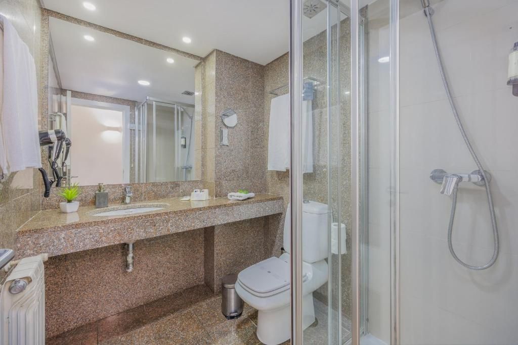 A modern bathroom with a granite countertop, a glass shower enclosure, and a white toilet.