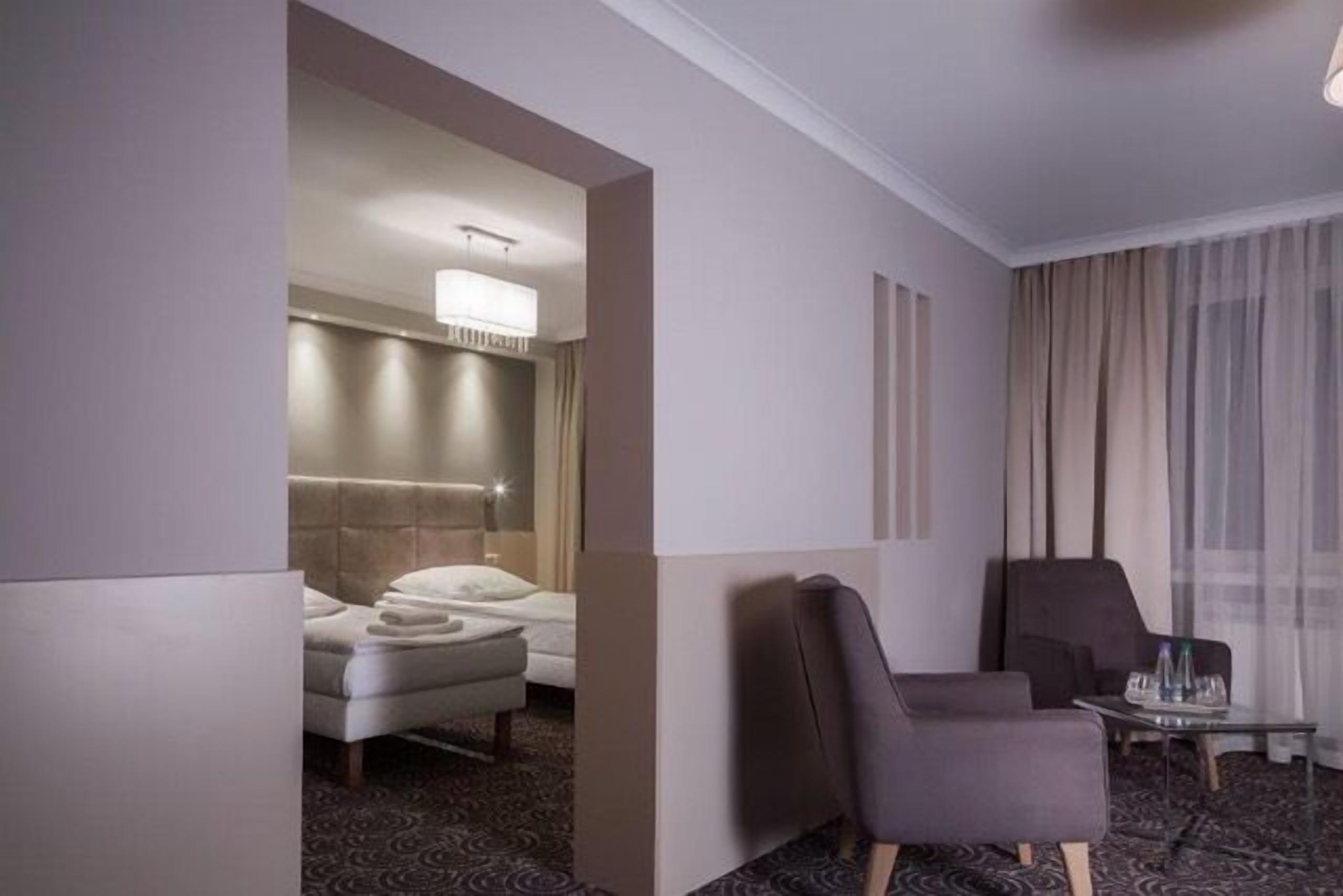A hotel room with a bed, a seating area with a chair and a small table, and a large window with curtains.