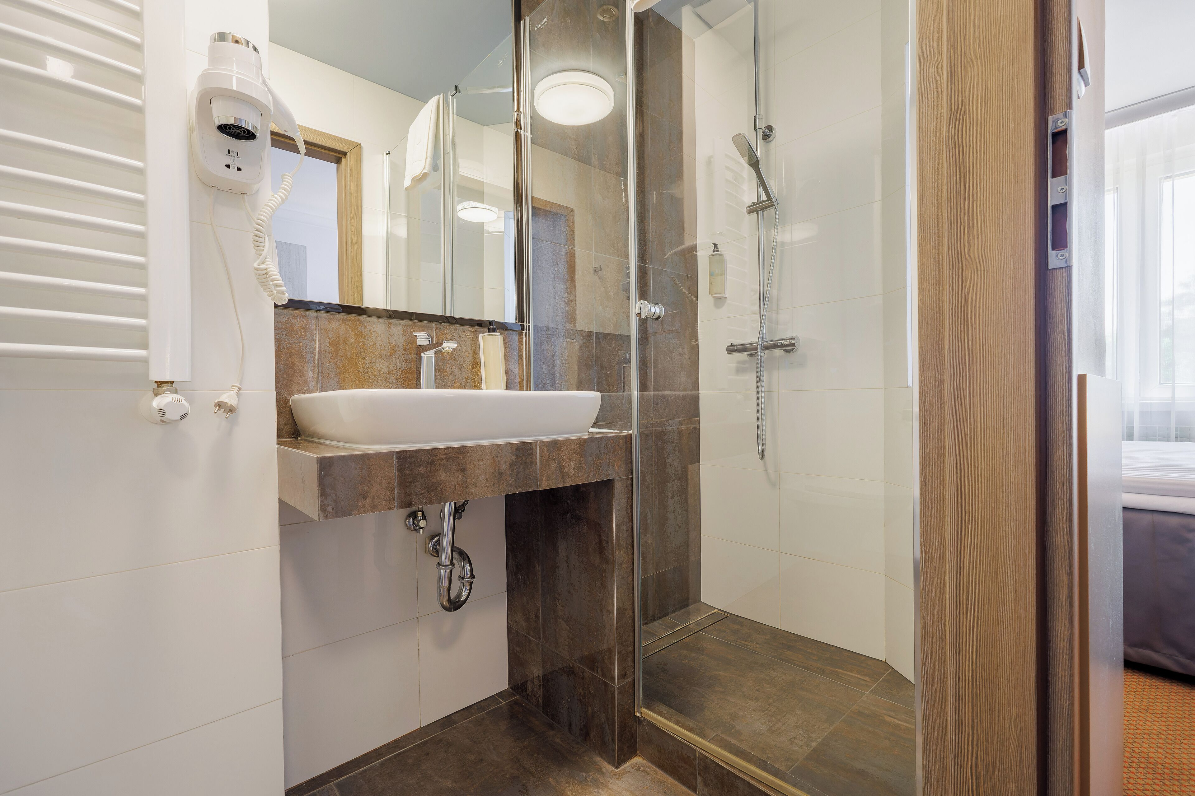 A modern bathroom with a glass-enclosed shower, a white sink, and a hairdryer mounted on the wall.