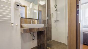A modern bathroom with a glass-enclosed shower, a white sink, and a hairdryer mounted on the wall.